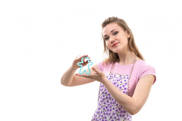 Foto grátis uma vista frontal jovem atraente dona de casa na capa rosa camisa colorida posando sorrindo segurando pouco azul humano formado brinquedo sobre o fundo branco cozinha cozinha