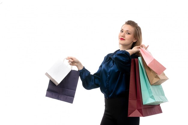 Uma vista frontal jovem atraente em blusa azul calça preta posando segurando pacotes de compras no fundo branco moda roupas elegantes