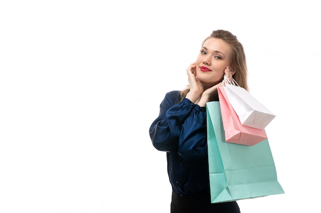 Foto grátis uma vista frontal jovem atraente em blusa azul calça preta posando segurando pacotes de compras sorrindo feliz no fundo branco moda roupas elegantes