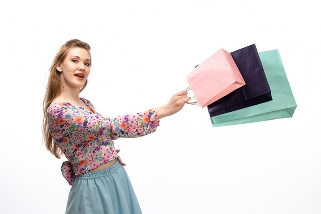 Foto grátis uma vista frontal jovem atraente em flor colorida projetada camisa e saia azul segurando pacotes de compras em branco