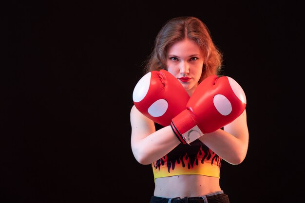 Uma vista frontal jovem atraente em luvas de boxe vermelhas fogo camisa sobre o treinamento de boxe de esporte de fundo preto