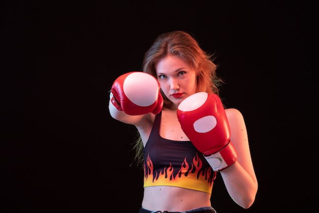 Uma vista frontal jovem atraente em luvas de boxe vermelhas fogo camisa sobre o treinamento de boxe de esporte de fundo preto