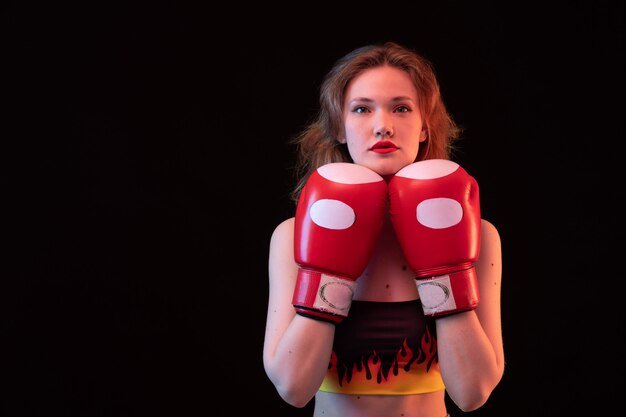 Uma vista frontal jovem atraente em luvas de boxe vermelhas fogo camisa sobre o treinamento de boxe de esporte de fundo preto