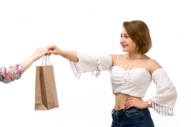 Uma vista frontal jovem atraente na camisa branca e calça jeans azul, tendo o pacote da fêmea sorrindo no branco