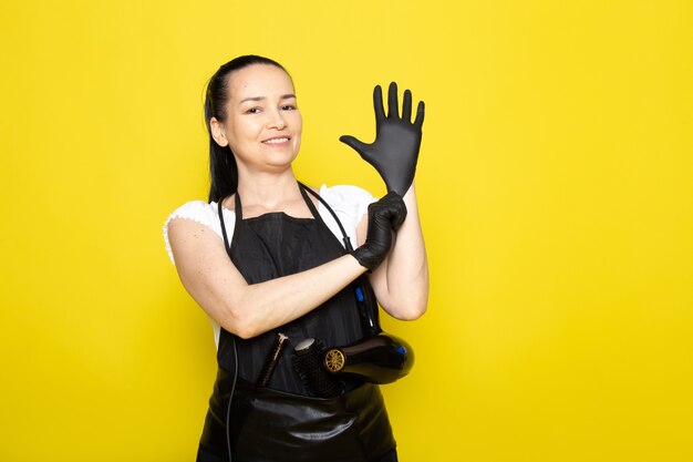 Uma vista frontal jovem cabeleireiro feminino na capa branca de camiseta preta em luvas pretas sorrindo