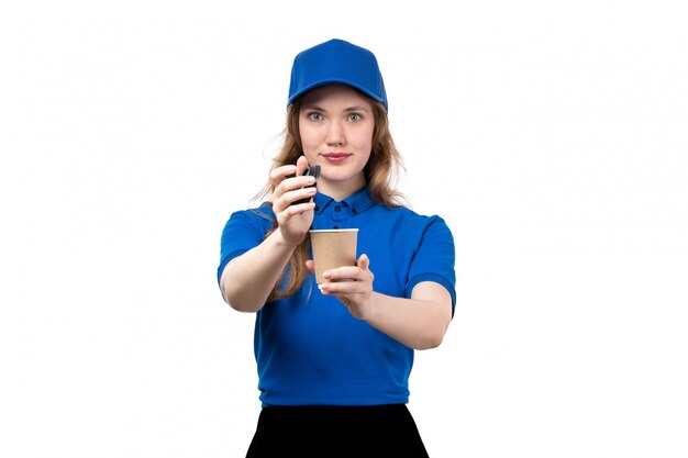 Uma vista frontal jovem correio feminino de camisa azul, boné azul e calça preta, segurando a xícara de café em branco