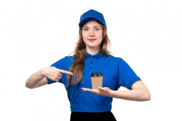 Uma vista frontal jovem correio feminino de camisa azul, boné azul e calça preta, segurando a xícara de café, sorrindo em branco