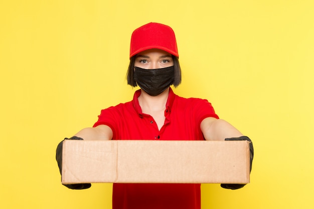 Uma vista frontal jovem correio feminino em luvas pretas uniformes vermelhas e boné vermelho segurando a caixa de alimentos