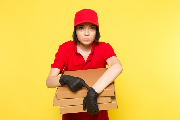 Uma vista frontal jovem correio feminino em luvas pretas uniformes vermelhas e boné vermelho segurando caixas de alimentos