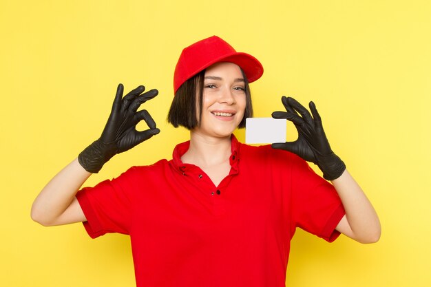 Uma vista frontal jovem correio feminino em luvas pretas uniformes vermelhas e boné vermelho segurando o cartão branco com sorriso