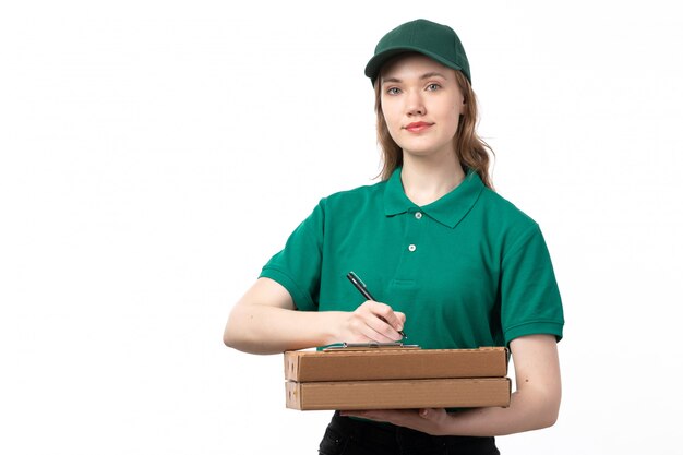 Uma vista frontal jovem correio feminino em uniforme verde segurando caixas com pizza, anotando novos pedidos em branco