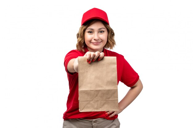 Uma vista frontal jovem correio feminino trabalhadora do serviço de entrega de comida segurando o pacote de alimentos sorrindo em branco