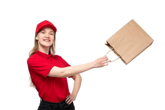 Uma vista frontal jovem correio feminino trabalhadora do serviço de entrega de comida sorrindo segurando o pacote de entrega de comida com ótimo humor em branco