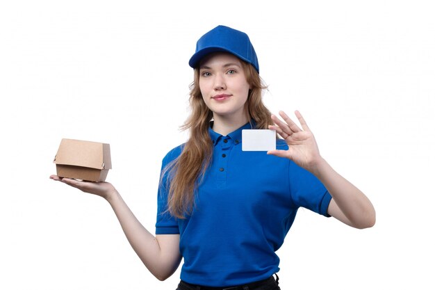 Uma vista frontal jovem correio feminino trabalhadora do serviço de entrega de comida sorrindo segurando pacote de entrega de comida e cartão branco no branco