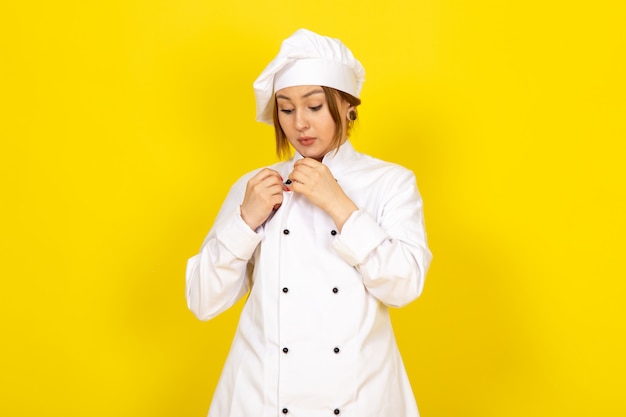 Uma vista frontal jovem cozinheira feminina no fato de cozinheiro branco e boné branco que fixa o terno no amarelo