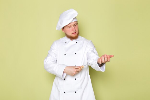 Uma vista frontal jovem cozinheiro masculino em branco cozinheiro terno branco cabeça tampa segurando a faca