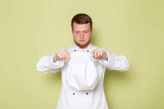 Foto grátis uma vista frontal jovem cozinheiro masculino em fato de cozinheiro branco tirando seu boné branco