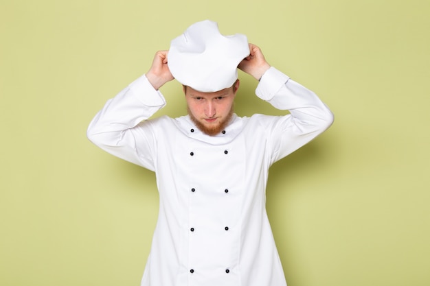 Foto grátis uma vista frontal jovem cozinheiro masculino em traje de cozinheiro branco usando boné de cabeça branca