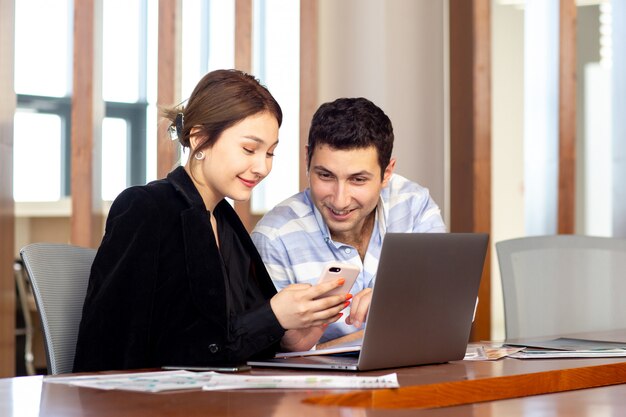 Uma vista frontal jovem empresária linda camisa preta jaqueta preta, juntamente com o jovem usando seu laptop prata discutindo questões dentro de seu escritório trabalho edifício de emprego