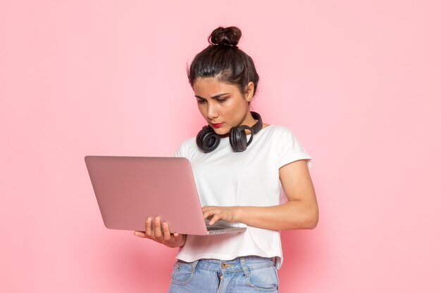 Uma vista frontal jovem fêmea em t-shirt branca e azul jeans usando laptop