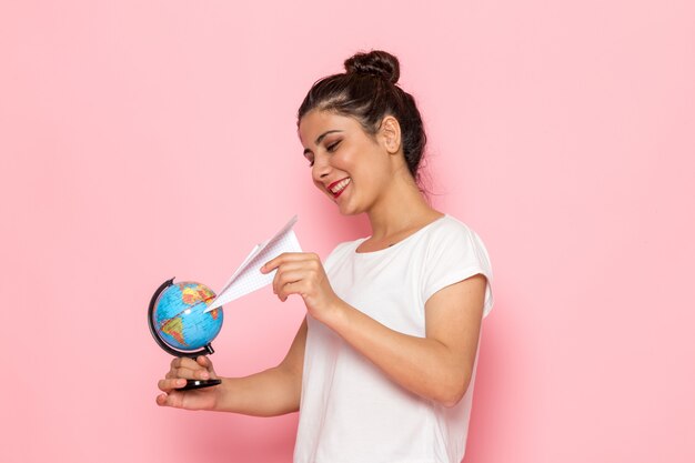 Uma vista frontal jovem fêmea em t-shirt branca e calça jeans azul, segurando o avião de papel e pequeno globo