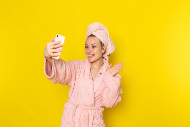 Foto grátis uma vista frontal jovem fêmea linda em roupão rosa tomando uma selfie com sorriso