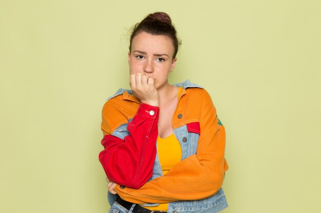 Uma vista frontal jovem fêmea na camisa amarela jaqueta colorida e azul jeans posando