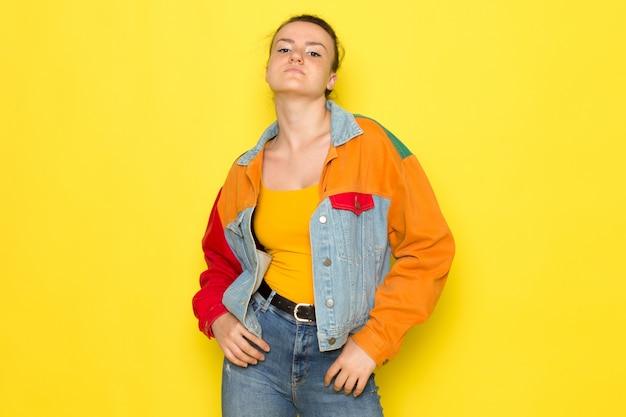 Uma vista frontal jovem fêmea na camisa amarela jaqueta colorida e jeans azul apenas boxe