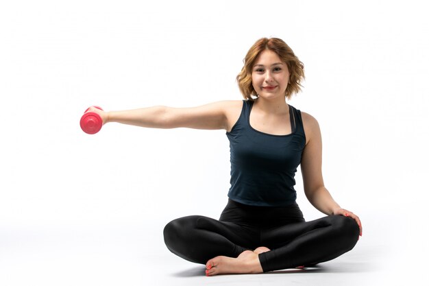 Uma vista frontal jovem garota atraente na camisa azul e calça preta esporte roupa fazendo exercícios sorrindo em branco