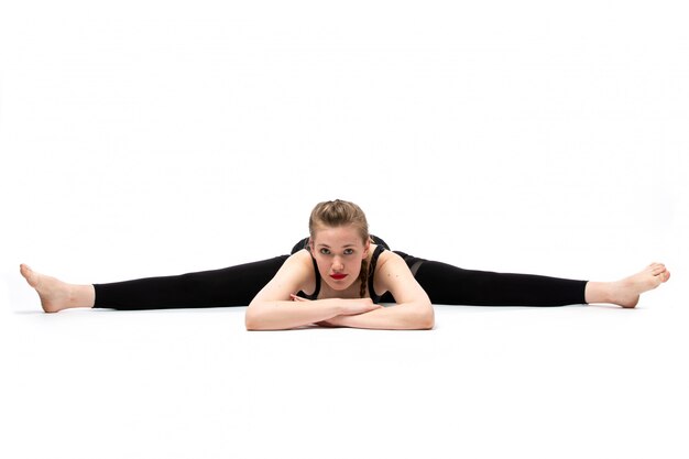 Uma vista frontal jovem garota bonita camisa esporte preta e calça preta posando fazendo ginástica em poses diferentes no branco