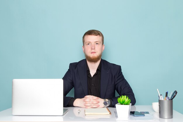 Uma vista frontal jovem homem atraente com barba no terno moderno clássico escuro preto no espaço azul