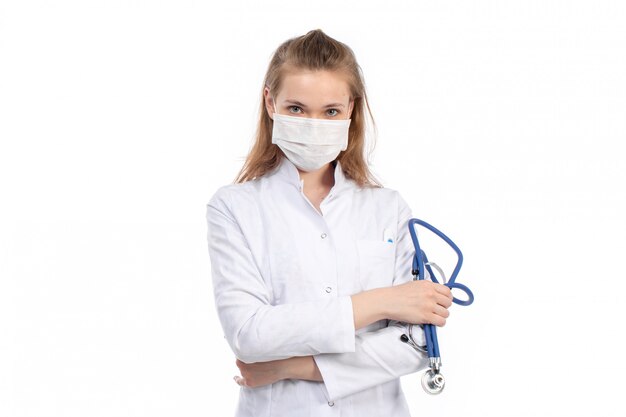 Uma vista frontal jovem médica em traje médico branco com estetoscópio usando máscara protetora branca sobre o branco