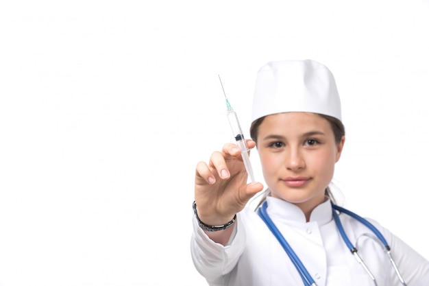 Uma vista frontal jovem médica em traje médico branco e boné branco com estetoscópio azul segurando a injeção