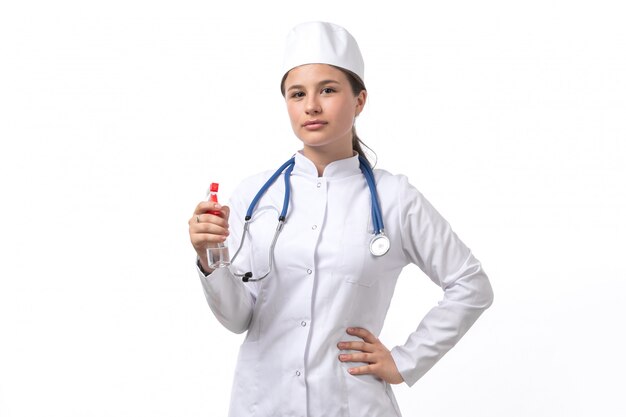 Uma vista frontal jovem médica em traje médico branco e boné branco com estetoscópio azul segurando o spray