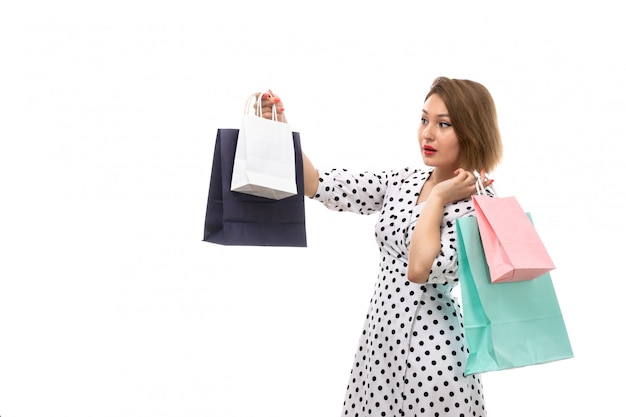 Uma vista frontal jovem mulher bonita no vestido de bolinhas em preto e branco segurando pacotes de compras surpresos