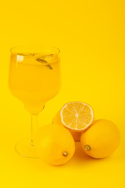 Uma vista frontal limões frescos amarelos frescos maduros inteiros e cortados com bebida de limão dentro de frutas de vidro isoladas sobre o fundo amarelo cor de frutas cítricas