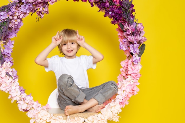 Uma vista frontal loira criança feliz na camiseta branca sentado na flor feita ficar na mesa amarela
