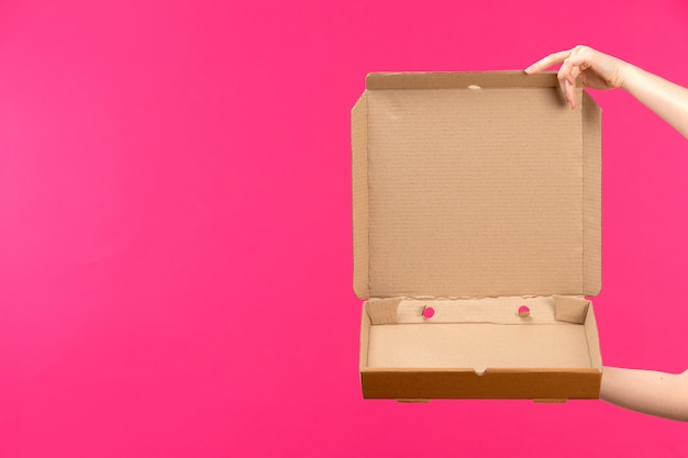 Foto grátis uma vista frontal marrom pacote vazio mão segurando pacote vazio mão feminina fundo rosa cor alimentos