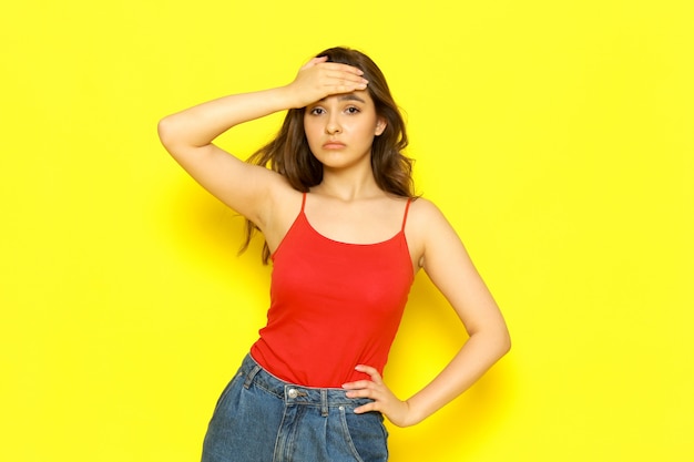 Uma vista frontal menina bonita camisa vermelha e calça jeans azul, posando com má expressão