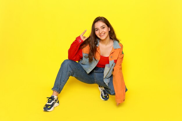 Uma vista frontal menina bonita no casaco de camisa vermelha e calça jeans azul posando com expressão sorridente