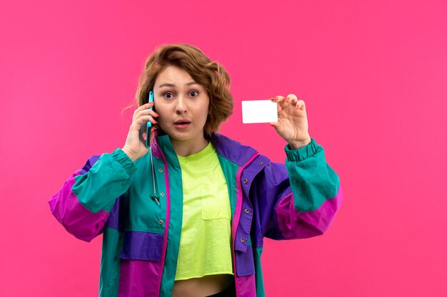 Uma vista frontal moça bonita em camisa colorida de ácido, calça preta, casaco colorido, falando ao telefone