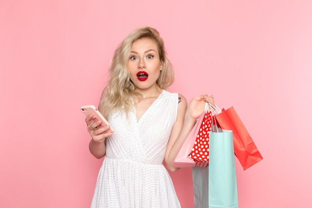 Uma vista frontal moça bonita no vestido branco segurando pacotes de compras, segurando um telefone