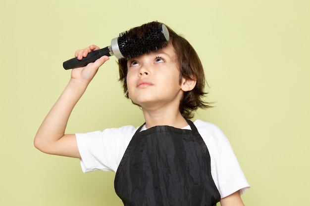 Uma vista frontal pequeno cabeleireiro criança adorável em capa preta posando