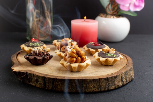 Uma vista frontal pequenos bolos com nozes e areia de chocolate na mesa de madeira e fundo escuro doce cor de bolo de açúcar