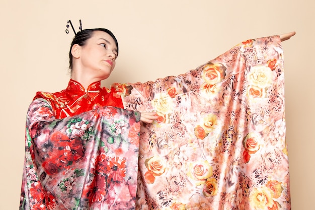 Foto grátis uma vista frontal requintada gueixa japonesa tradicional vestido japonês vermelho posando com tecido projetado de flores elegante sobre a cerimônia de creme de fundo japão