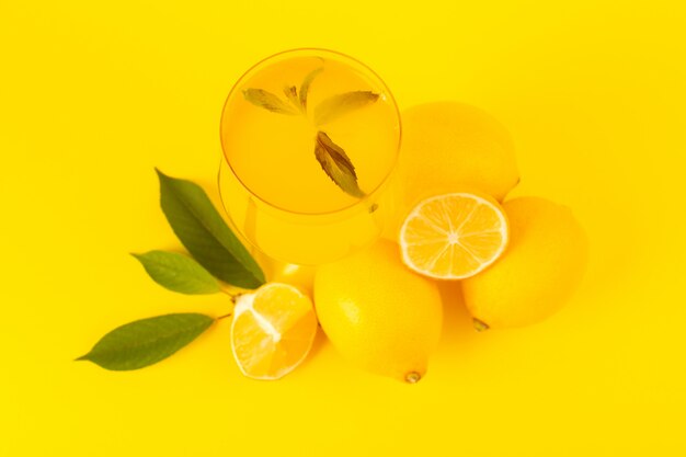 Uma vista superior amarelo limões frescos frescos maduros inteiros e fatiados com bebida de limão dentro de frutas de vidro isoladas sobre o fundo amarelo cor de frutas cítricas