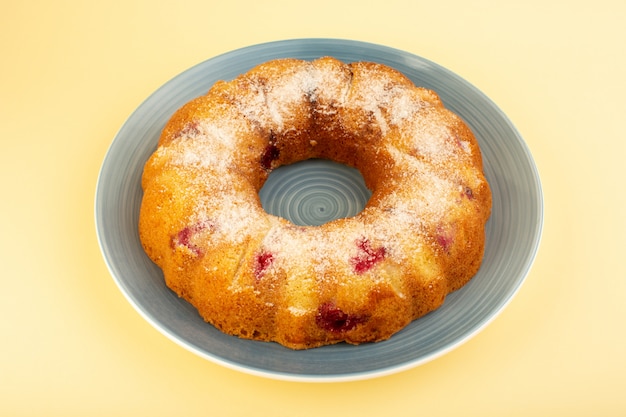 Uma vista superior assada de bolo de frutas delicioso redondo com cerejas vermelhas dentro e açúcar em pó dentro de um prato redondo amarelo