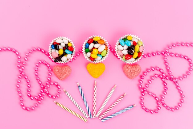 Uma vista superior de doces coloridos dentro de pacotes de papel, juntamente com velas e joias em rosa