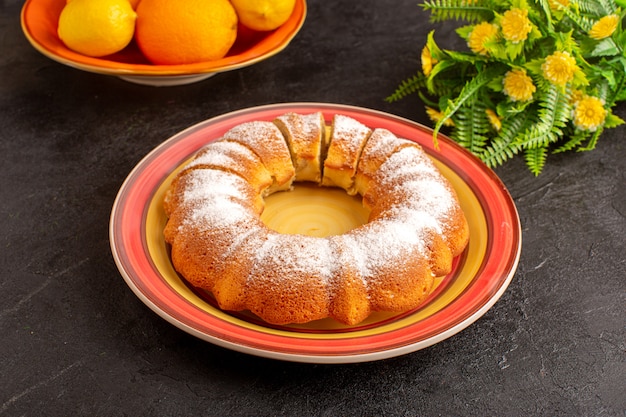 Uma vista superior doce redondo bolo com açúcar em pó fatiado doce delicioso bolo isolado dentro da placa junto com limões e fundo cinza biscoito de açúcar