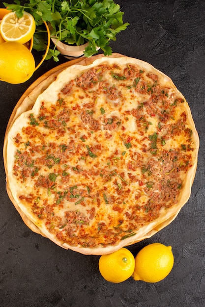 Uma vista superior lahmacun massa com carne picada, juntamente com verduras e limão dentro de caixa de papel saborosa refeição de pastelaria